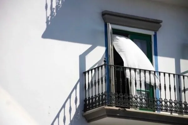 Balkon an einer weißen Hauswand, ein weißer Vorhang weht aus der offenen Tür