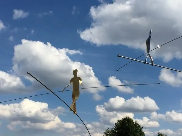 Skulpturen von Seiltänzern vor einem Wolkenhimmel
